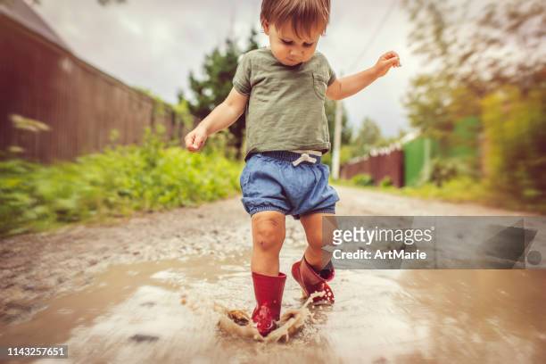 little boy playing in puddle in a rainy day - russia rain boots imagens e fotografias de stock