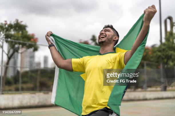 male fan celebrating and holding brazilian flag - brazilian ethnicity stock pictures, royalty-free photos & images