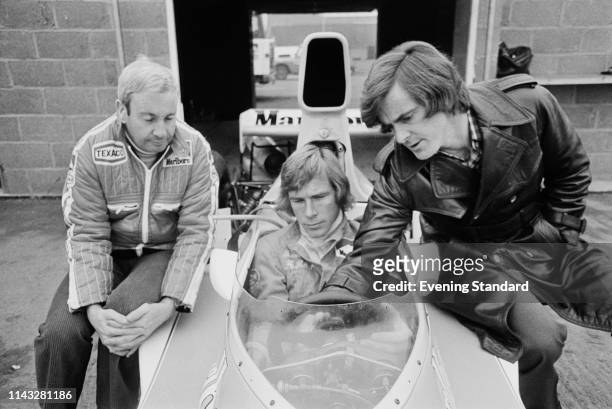 British racing driver James Hunt sitting at the wheel of the M26 Marlboro McLaren racing car at Silverstone with Teddy Mayer, racing director sits to...