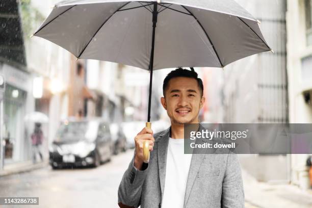 young chinese man with umbrella - asia rain stock pictures, royalty-free photos & images