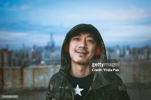 portrait of man using headphones listening music and looking at camera with smile on rooftop of tall building, shanghai, china - solo un uomo di età media foto e immagini stock