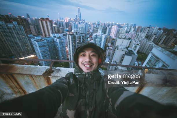 selfie portrait of man using headphones and looking at camera with smile on rooftop of tall building, shanghai, china - chinese people posing for camera stockfoto's en -beelden