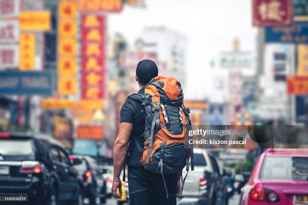 Backpacker looking at the street in the chinatown of Bangkok in Thailand during day .
