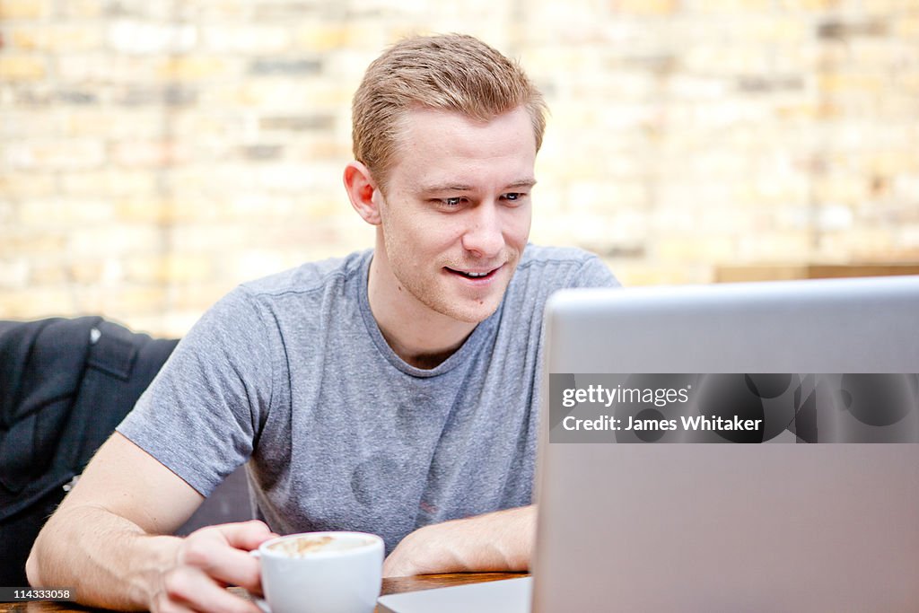 Man Reads Laptop Outside with Coffee