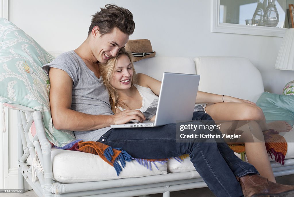 Couple snuggling on the sofa, looking at laptop