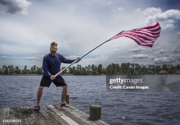 cheerful man waving american flag while standing on pier over lake against cloudy sky at banff national park - vlag planten stockfoto's en -beelden