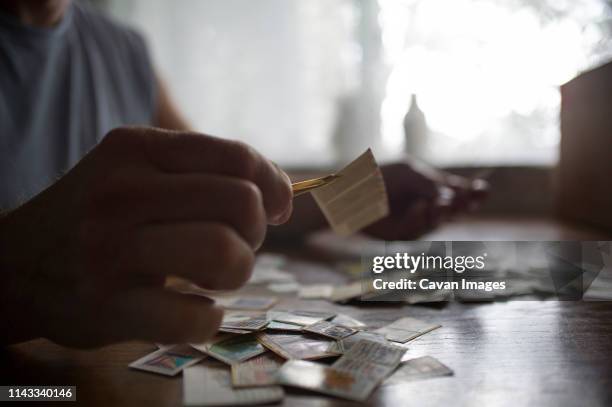 close-up of man holding postage stamps with tweezers on table at home - collect stamps stock pictures, royalty-free photos & images