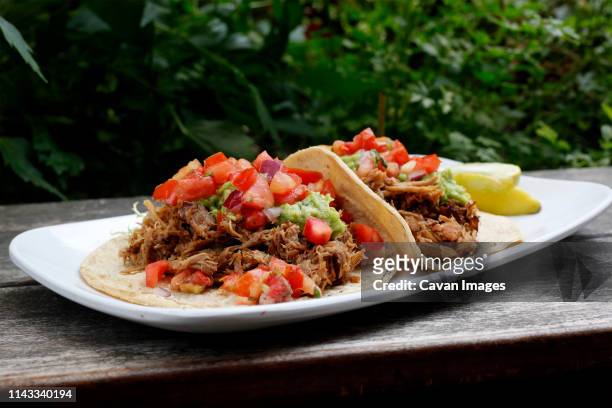 close-up of tacos served in plate on wooden table against plants - mexican food plate stock pictures, royalty-free photos & images