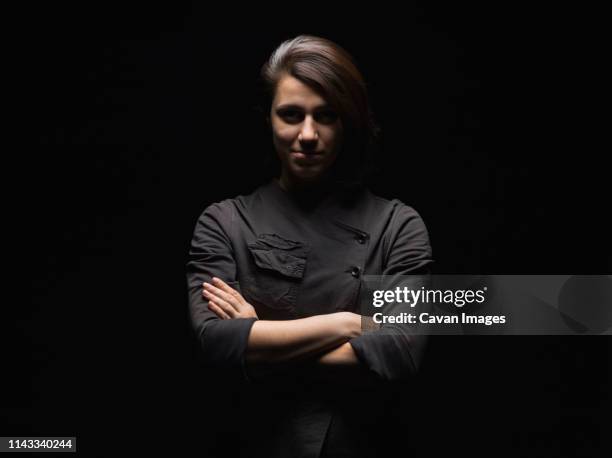 portrait of confident woman with arms crossed standing against black background - studio portrait dark background stock-fotos und bilder