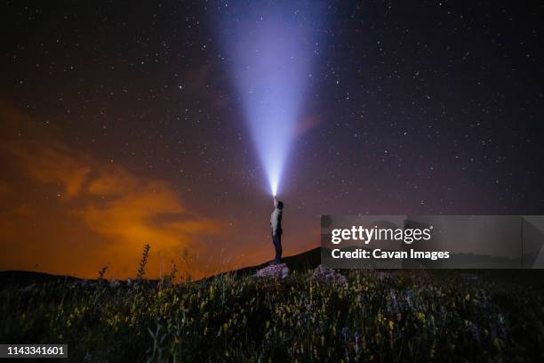 side view of man holding illuminated flashlight while standing on hill against star field at night - electric torch stock pictures, royalty-free photos & images