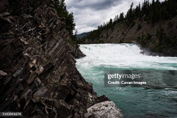 scenic view of river flowing amidst mountains against cloudy sky - fort mcmurray stock pictures, royalty-free photos & images