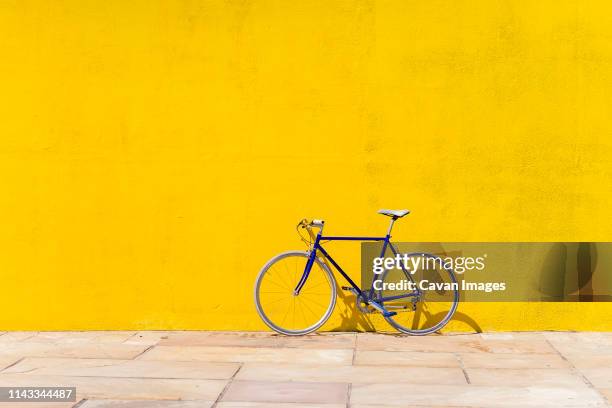 bicycle parked on sidewalk by wall during sunny day - yellow wall stockfoto's en -beelden