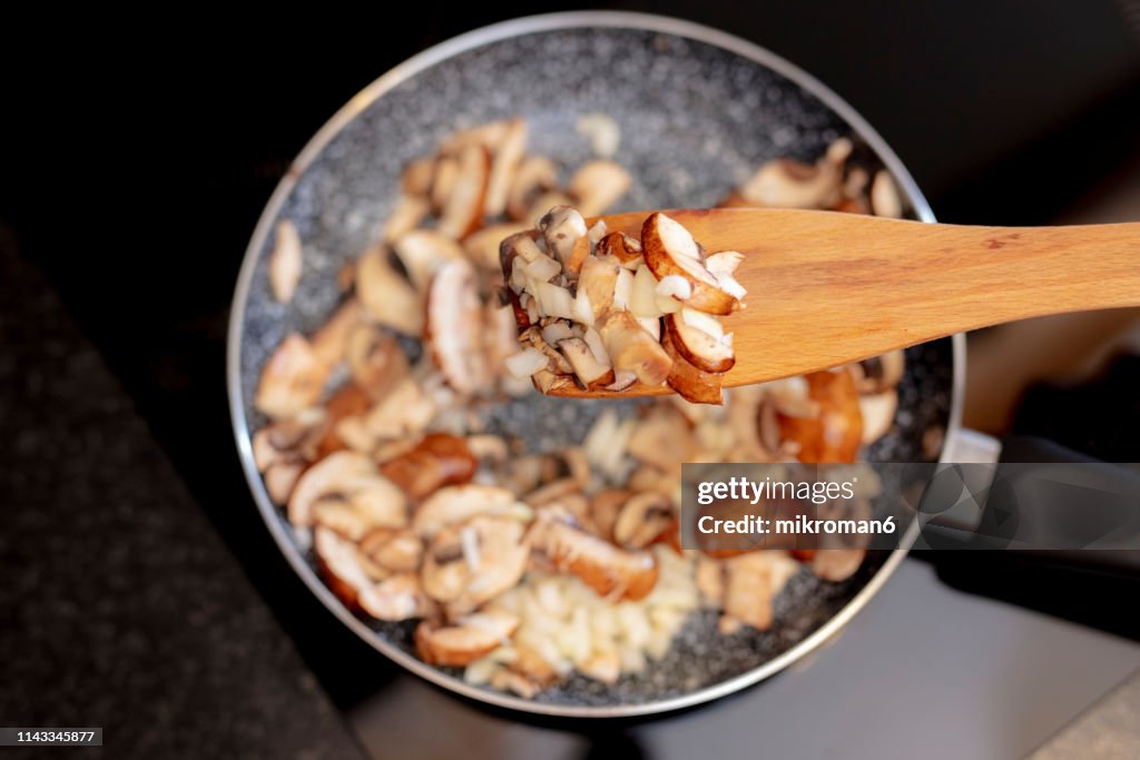 Woman stirring sliced brown mushrooms in frying pan