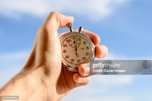 cropped hand of man holding stopwatch against sky - stop watch stock pictures, royalty-free photos & images