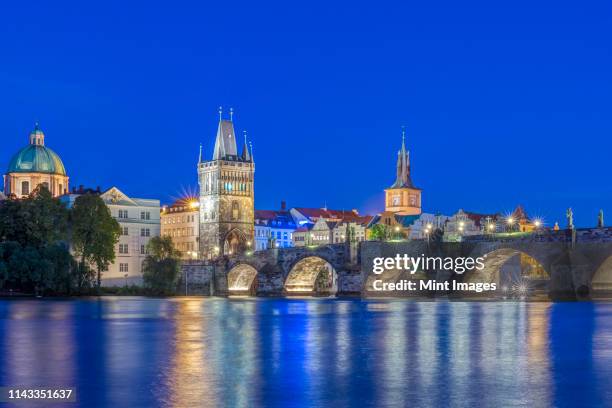 charles bridge and city illuminated at dusk, prague, czech republic - prague river stock pictures, royalty-free photos & images