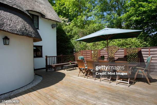 table and chairs on cottage patio - strohdach stock-fotos und bilder