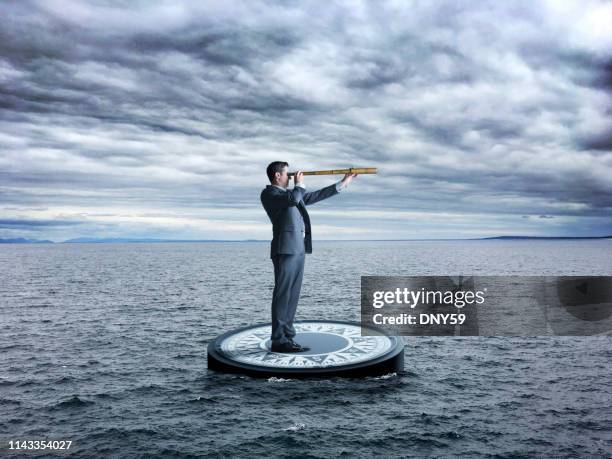 businessman stands on compass looking through spyglass in stormy seas - looking through an object stock pictures, royalty-free photos & images