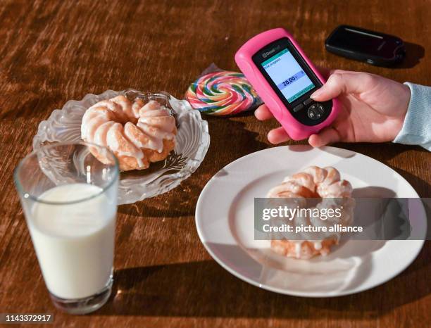 February 2019, Berlin: ILLUSTRATION - A girl is holding a remote control for the mylife Omnipod tubeless insulin pump next to plates with cake, milk...