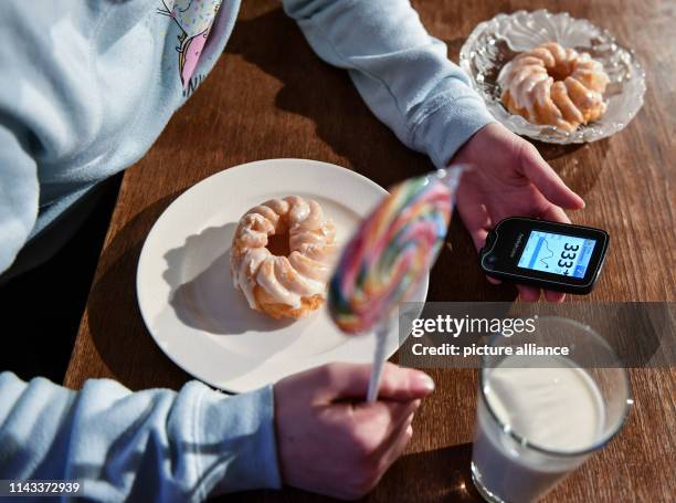 February 2019, Berlin: ILLUSTRATION - A girl is holding a Freestyle Libre blood glucose meter with far too high a blood glucose level next to plates...