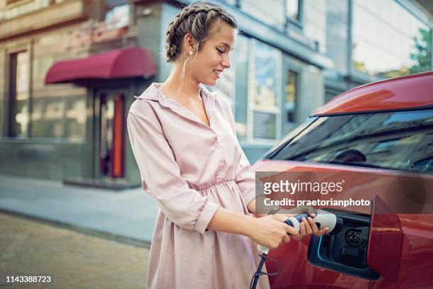 young girl is charging her electric car in the city - recharging stock pictures, royalty-free photos & images
