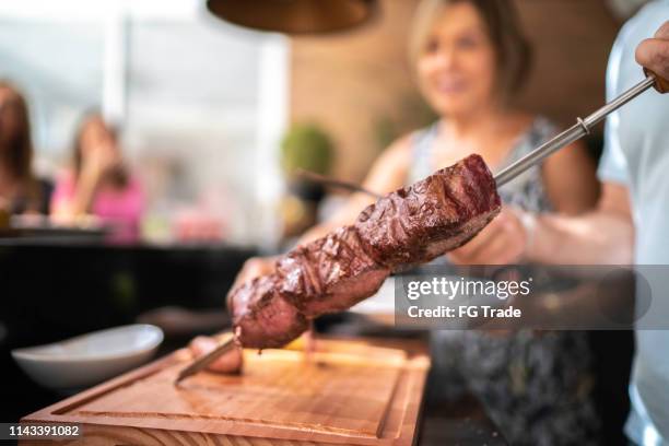 concéntrese en la carne de picanha de corte de mano del hombre durante la barbacoa - cultura-brasileira fotografías e imágenes de stock