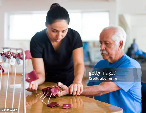 leiterkranker, der die hand mit physiotherapie-gerät trainiert - occupational therapist stock-fotos und bilder