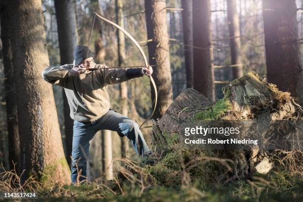 man shooting with bow and arrow in the forest, bavaria, germany - arrow bow and arrow stockfoto's en -beelden