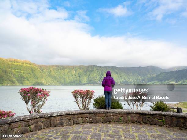 woman on top of a mountain in a lookout overlooking a volcanic landscape with lake. sao miguel island, azores islands, portugal. - uitkijktoren stockfoto's en -beelden