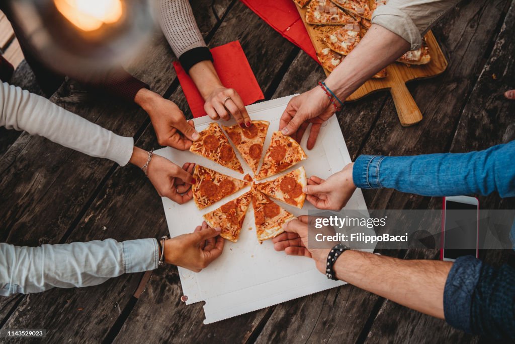 Friends taking a slice of pizza from the pizza box