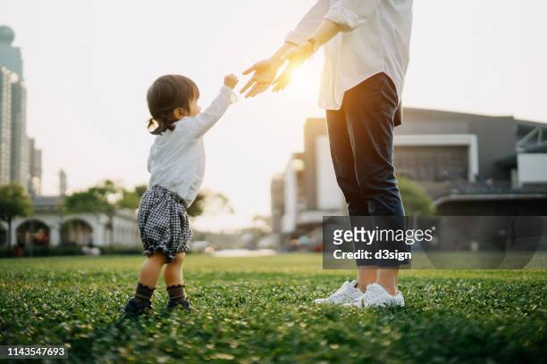 mother opening her arms out as daughter approaches in the park at sunset - park family sunset stock pictures, royalty-free photos & images
