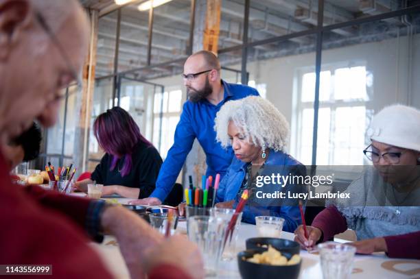 mixed group of people at a hand lettering workshop, teacher is helping - 50s woman writing at table stock-fotos und bilder