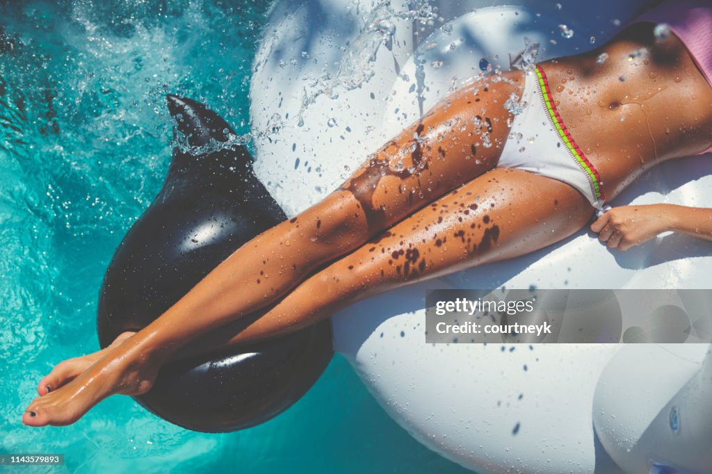 Woman floating on a white inflatable in swimming pool in a white bikini.