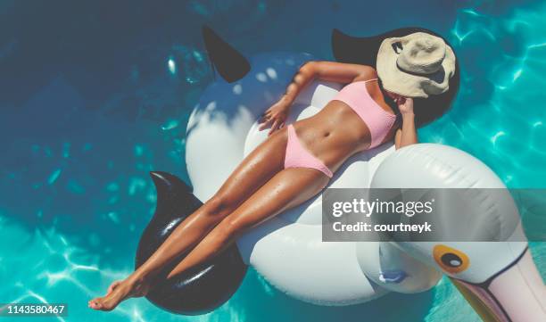 woman floating on a white inflatable in swimming pool in a pink bikini. - tanned body stock pictures, royalty-free photos & images
