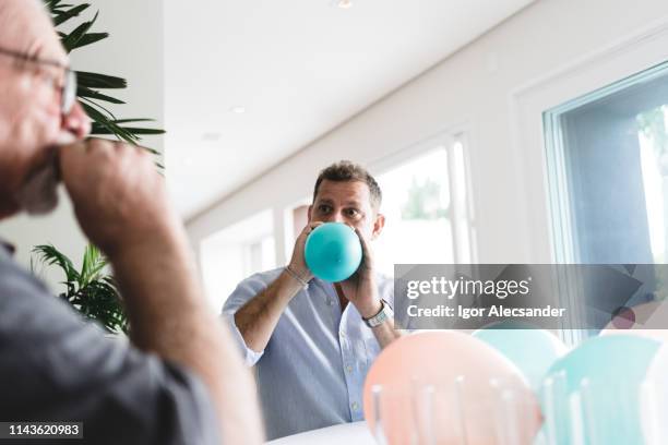 hombre soplando globo de fiesta - inflar fotografías e imágenes de stock
