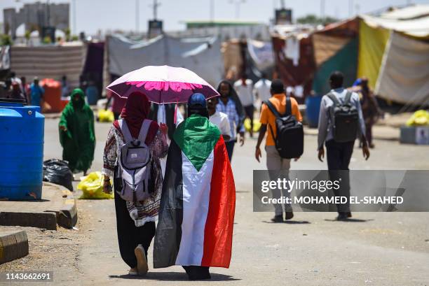 Sudanese woman walks draped in a national flag with another protester beneath an umbrella at the protest outside the army headquarters in the capital...