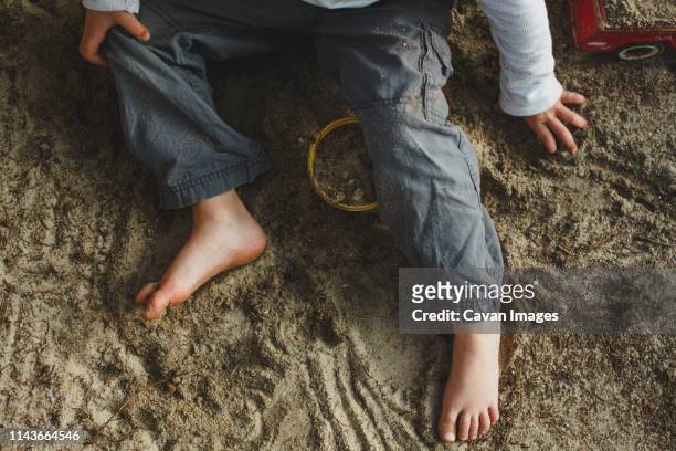 the bottom half of a small boy playing barefoot in a sandbox - sandkasten stock-fotos und bilder