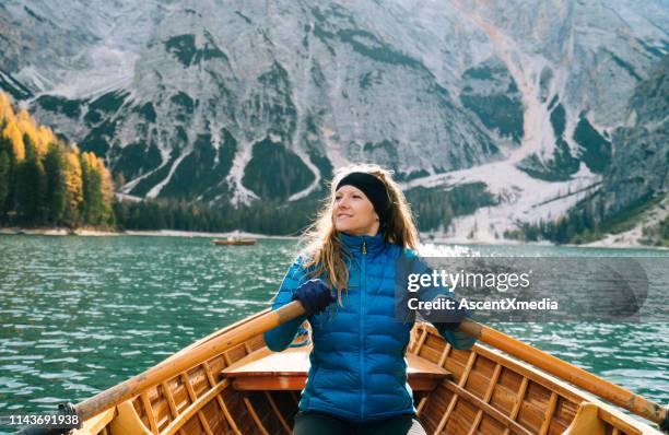 woman in row boat paddles toward mountain - down coat stock pictures, royalty-free photos & images