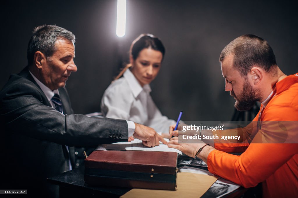 Man with handcuffs signing document in interrogation room