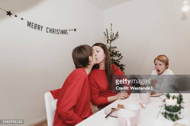same sex family celebrating christmas at home, women kissing - same person different outfits stock-fotos und bilder