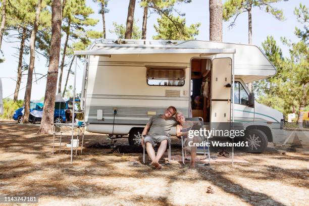 france, gironde, happy couple sitting in front of camper on camping ground - couple travel tablet stock-fotos und bilder