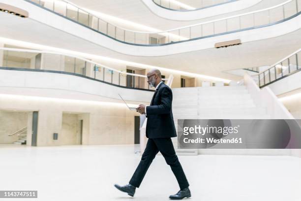 smart mature businessman using laptop while walking through foyer - business man walking photos et images de collection