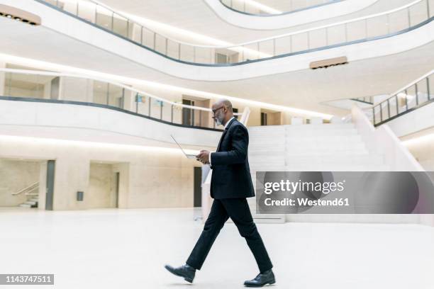 smart mature businessman using laptop while walking through foyer - business man walk stockfoto's en -beelden