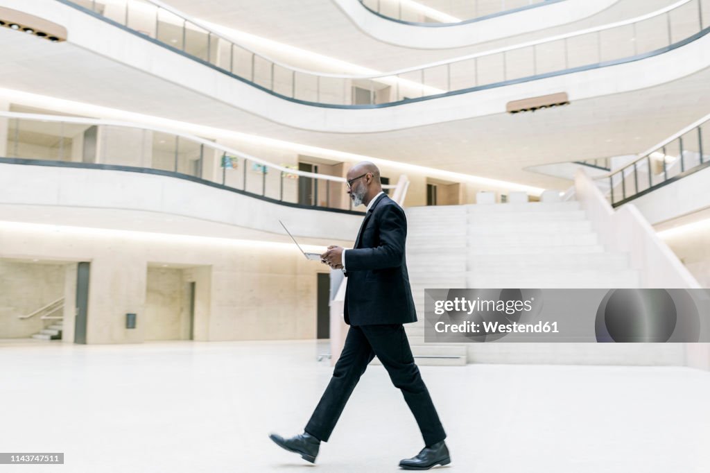 Smart mature businessman using laptop while walking through foyer