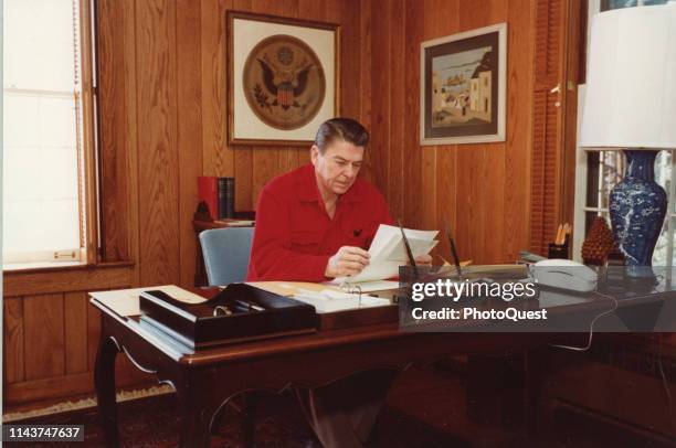 View of American politician US President Ronald Reagan as he reads documents at a desk looks during a presidential retreat at Camp David, Camp David,...