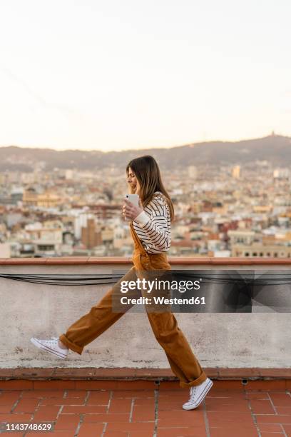happy young woman with smartphone walking on roof terrace - barcelona free stockfoto's en -beelden