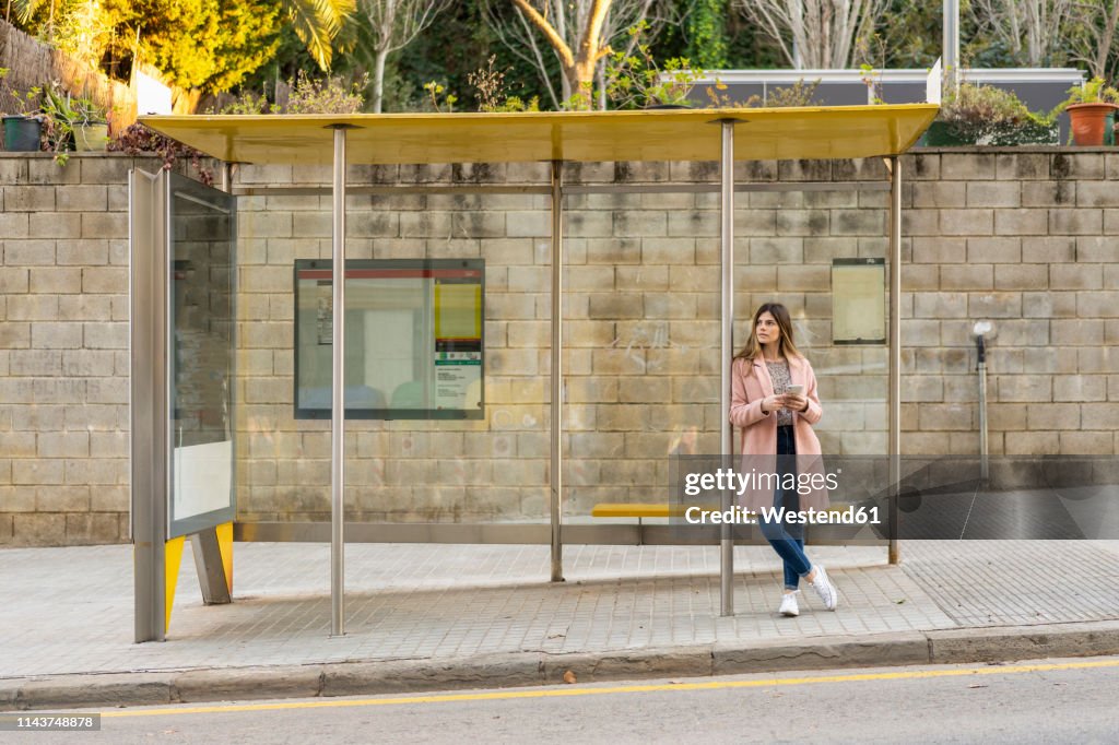 Young woman with cell phone waiting at bus stop