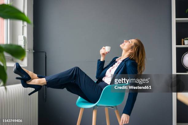 businesswoman taking a break, sitting on a chair next to the window, drinking coffee - pause café imagens e fotografias de stock
