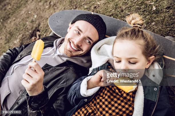father and daughter resting on skateboard, eating ice cream - father and child stock-fotos und bilder