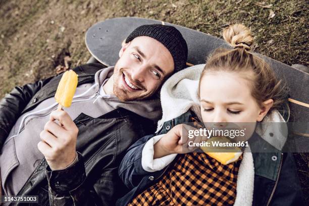 father and daughter resting on skateboard, eating ice cream - eating icecream stock pictures, royalty-free photos & images