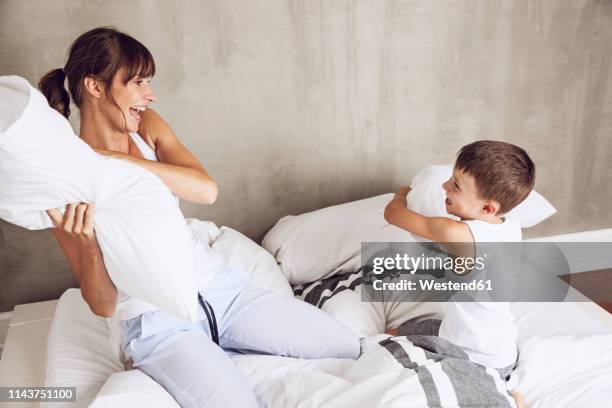 mother and son having fun, having a pillow fight in bed - kissenschlacht stock-fotos und bilder